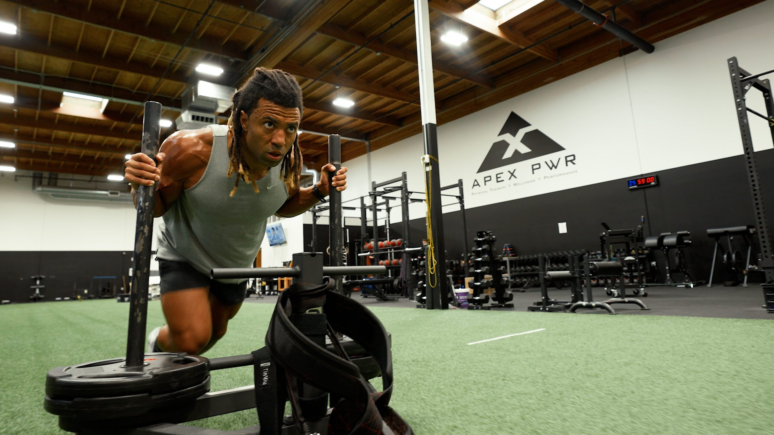 Athlete pushing loaded sled on turf during a Hyrox simulation in Portland at APEX PWR Tigard — APEX PWR facility and logo visible in background