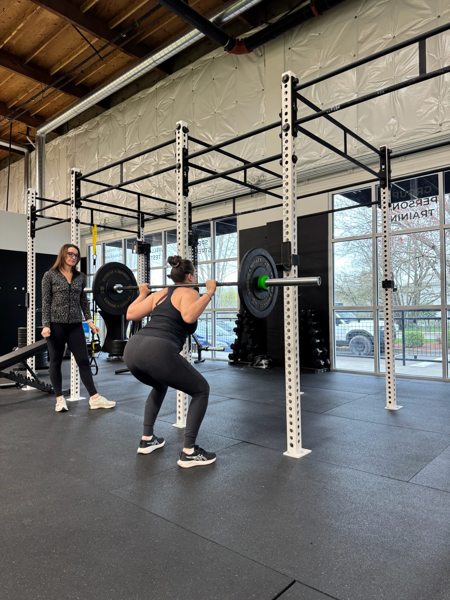 Female athlete back-squatting with a coach spotting at APEX PWR strength training facility in Tigard, Oregon