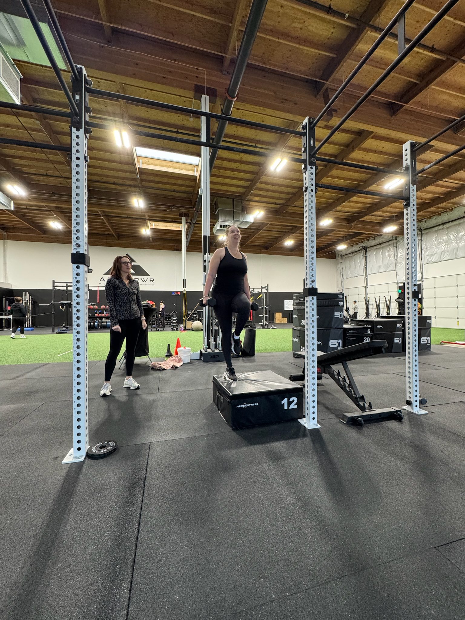 Female athlete performing dumbbell step-ups with coaching at APEX PWR personal training facility in Tigard, Oregon