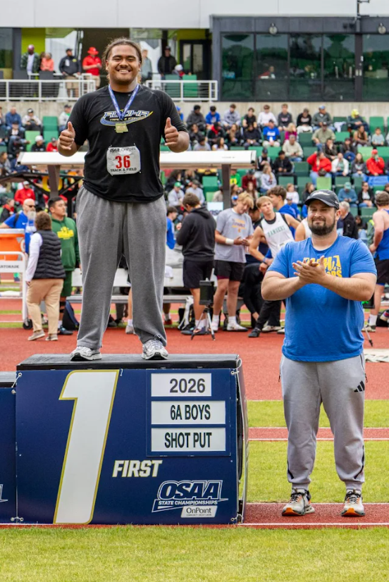 Aloha High School's Scottland Telesa stands atop the first-place podium in the 6A boys shot put at the 2026 OSAA State Championships, with Aloha throws coach and APEX Director of Rehab Dr. Jon van den Boogaard, DPT, OCS, USATF Level 2, alongside.
