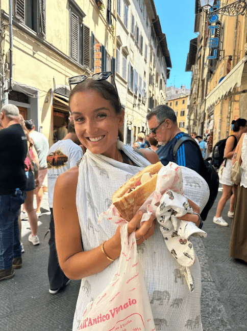 Jennie Carolan holding her son Oslo while eating a sandwich on a street in Florence, Italy during their family vacation